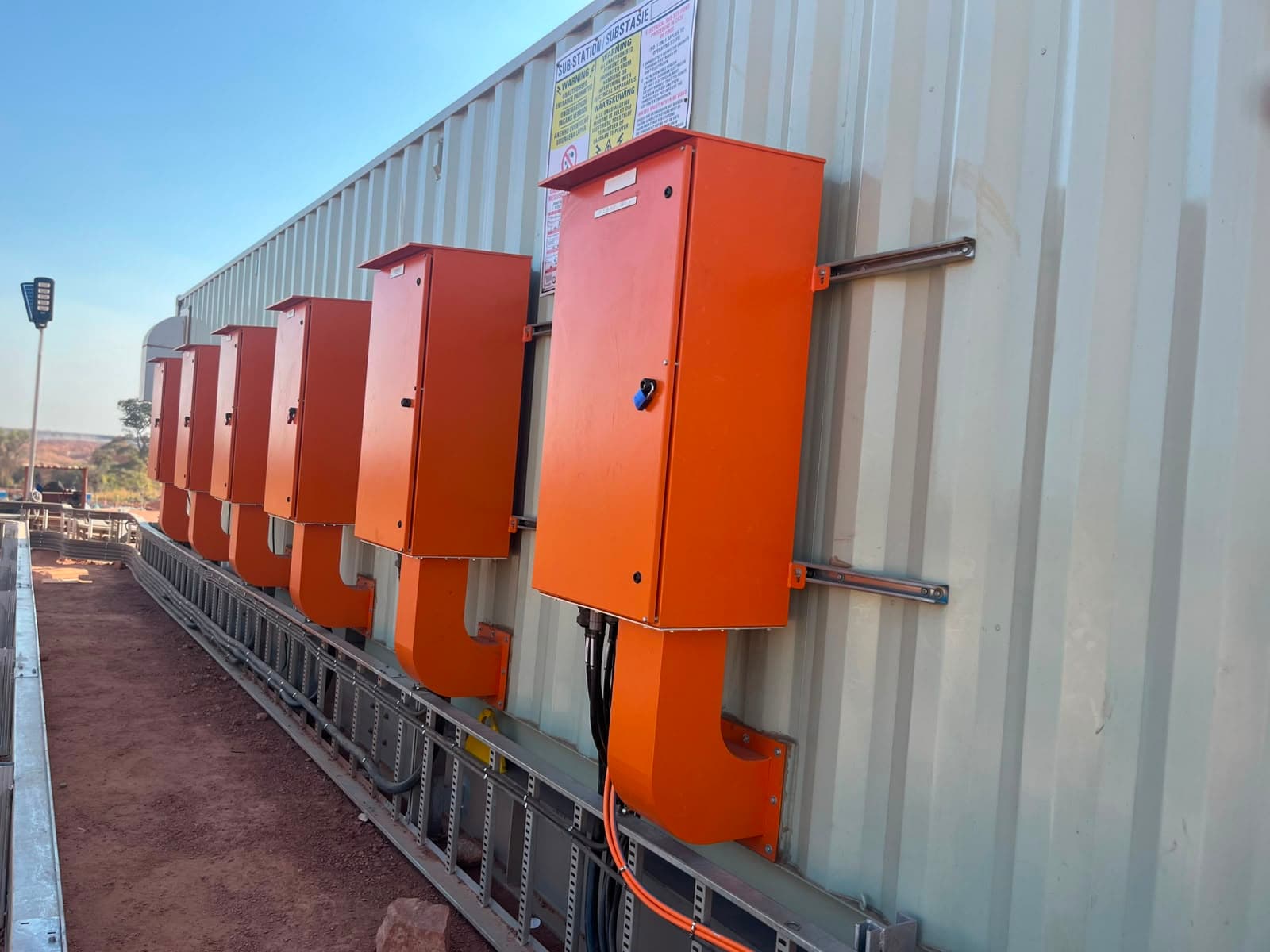 Orange Ivevane control enclosures mounted along a substation building on an industrial site under a clear sky.