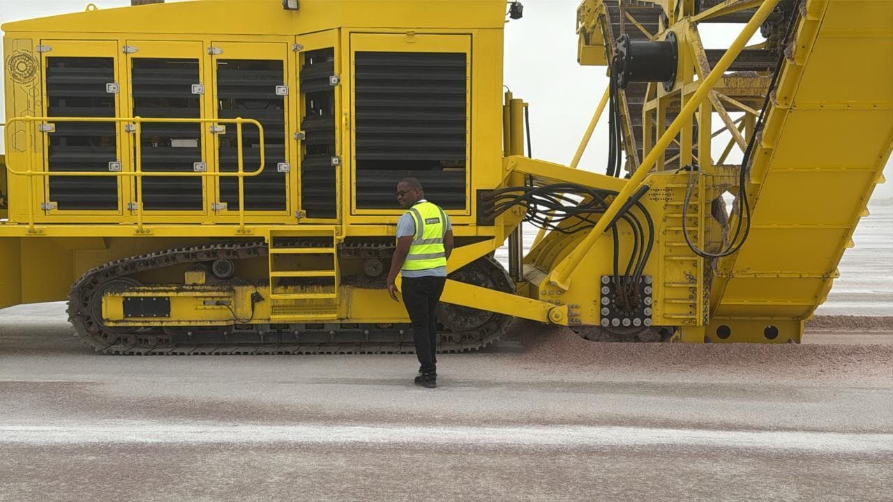 Salt harvester on tracks during a machine test run, with an engineer in a hi-vis vest beside it