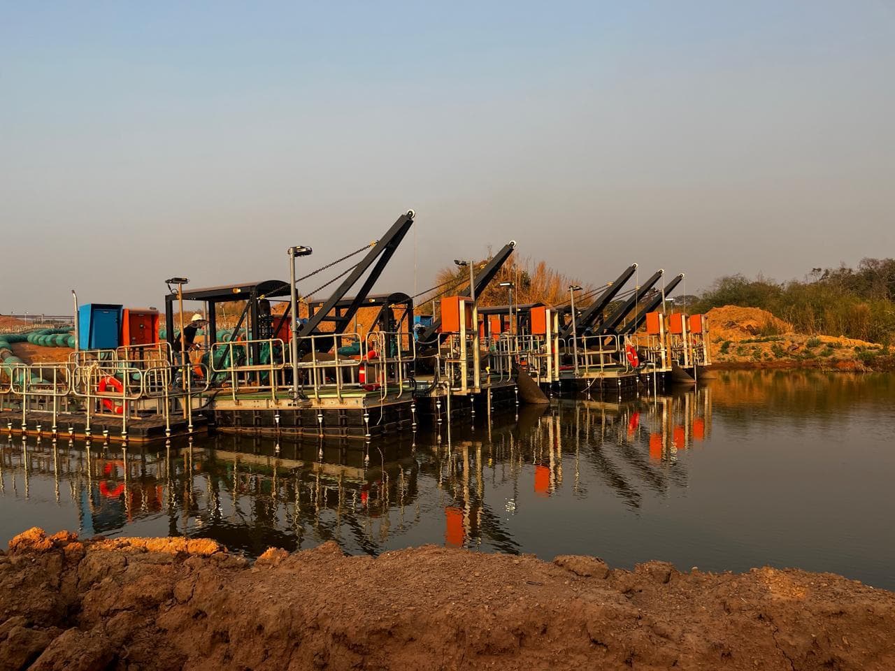 Row of pumping barges on a tailings water dam at sunset