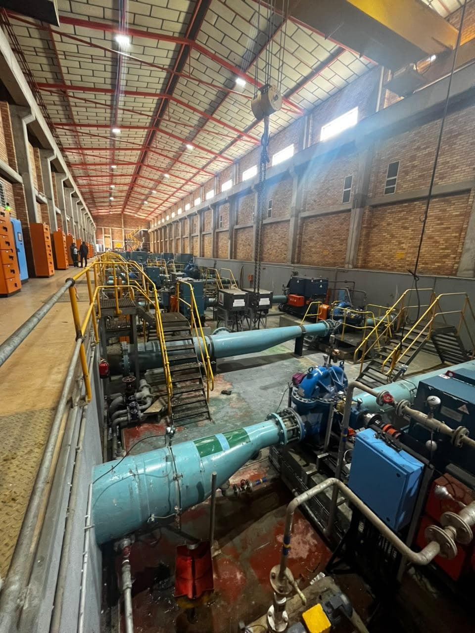Interior of a large pump house with pipework, pumps and a row of control panels